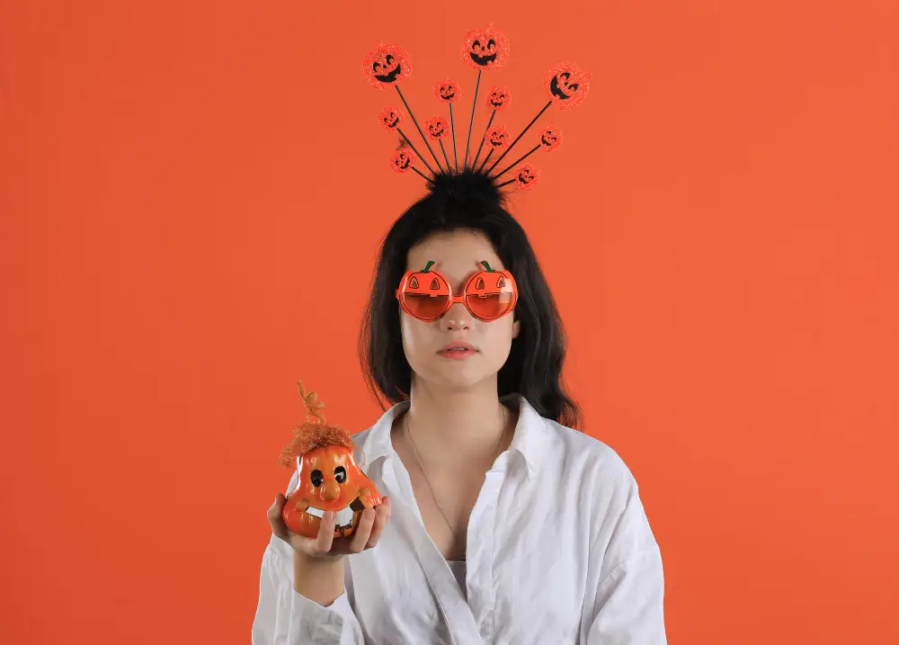 Young girl wearing festive Halloween makeup and spooky headband against an orange backdrop
