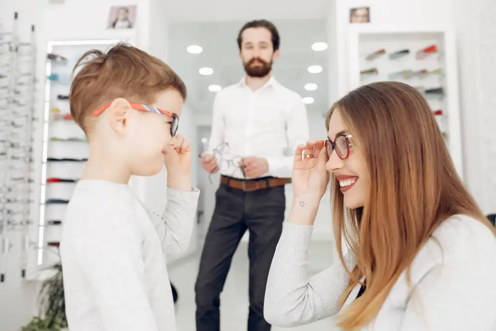 Mother helping her young son try on glasses at an optical store.